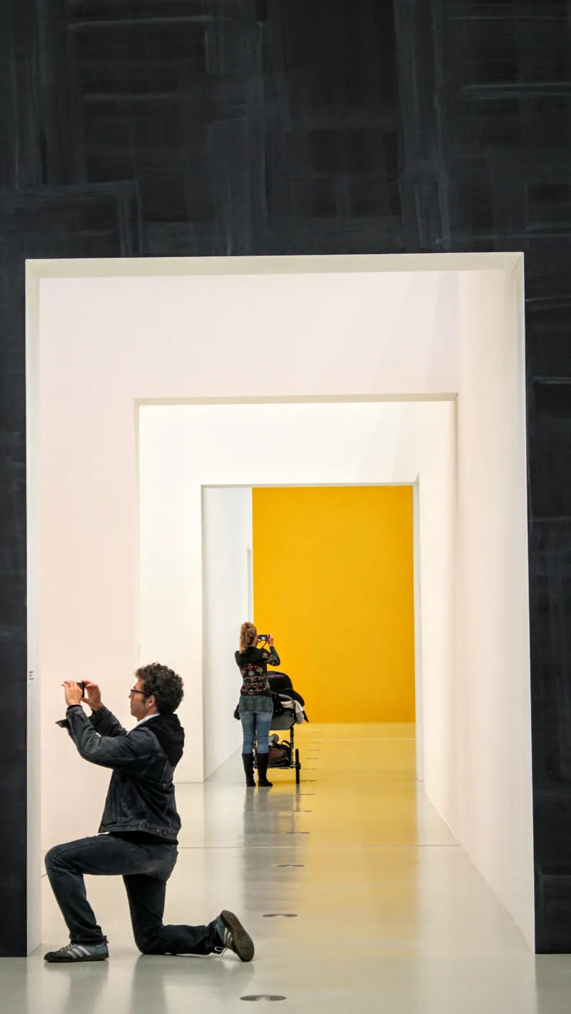 A visitor photographing a yellow wall at the end of nested white passages